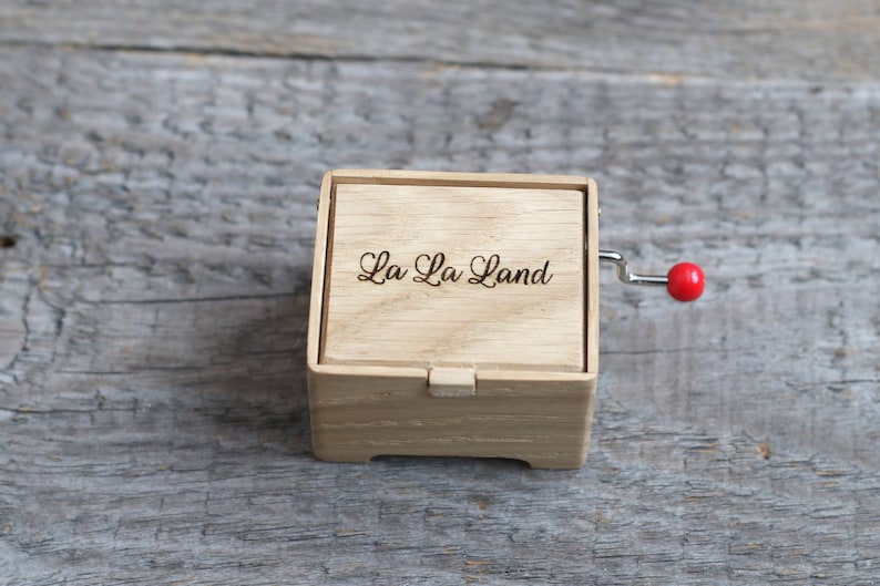 May include: A wooden music box with a red crank and the words "La La Land" engraved on the top.