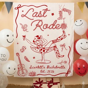 May include: A white fabric banner with red illustrations and text. The banner features a cowgirl in a martini glass, the words "Last Rodeo," and "Scarlett's Bachelorette Est. 2026." Decorative elements include a snake, dice, and a guitar. Balloons surround the banner.