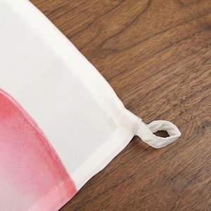 May include: Close-up of a white and pink fabric with a loop. The fabric has a watercolor-like design with shades of pink and red. The loop is made of the same white fabric.