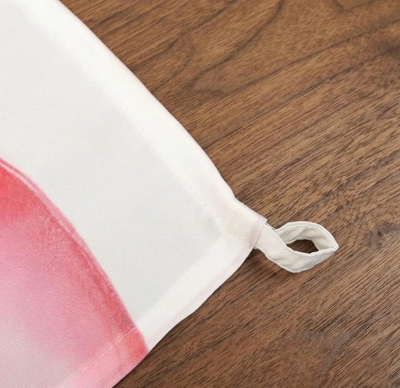 May include: Close-up of a white and pink fabric with a loop. The fabric has a watercolor-like design with shades of pink and red. The loop is made of the same white fabric.