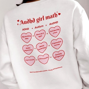以下が含まれることがあります： 赤い文字で「Audhd girl math」と書かれた白いスウェットシャツ。 下には、ADHD + 自閉症 = Audhdというピンクのハートの図があります。 スウェットシャツの下部には「best handled with snacks, clarity and patience」と書かれています。