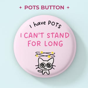 May include: A round, light pink button featuring the black text I have POTS and the pink text I CAN'T STAND FOR LONG. Below the text is a black line drawing of a cat with yellow stars circling its head, indicating dizziness or confusion.