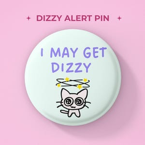 以下が含まれることがあります： 薄緑色の背景に紫色の文字で「I MAY GET DIZZY」と書かれた丸いピンバッジ。大きな目をした白い猫のイラストの頭上に黄色い星が回っているデザイン。ピンの上部には「DIZZY ALERT PIN」という文字が記載されている。