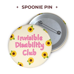Può includere: Una spilla rotonda con sfondo color crema caratterizzata da un motivo di girasoli gialli con foglie verdi. Il testo "Invisible Disability Club" è stampato al centro in lettere rosa arrotondate. Il retro mostra una spilla in metallo.