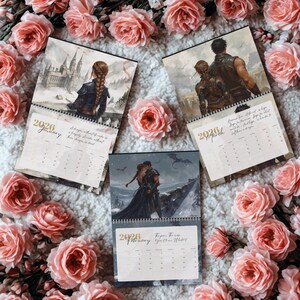 May include: Three 2026 wall calendar pages featuring fantasy illustrations of characters in armor and gowns, with one page showing a castle, another a couple, and the third a pair in a snowy landscape, all surrounded by pink roses.