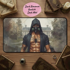 May include: A rectangular desk mat with a dark romance theme. The mat features a muscular figure wearing a hooded jacket and gas mask, with a spider tattoo on the chest. The background shows a building and spiderwebs. Text on the mat reads "Dark Romance Bookish Desk Mat."