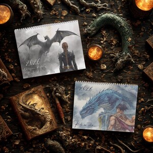 May include: Two spiral-bound 2026 wall calendars featuring fantasy dragon illustrations. One calendar shows a dark dragon and a person with a braided hairstyle, labeled 2026 Dragon Rider Calendar. The other shows a blue dragon and a person, labeled 2026 Ride or die.
