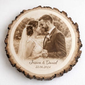 Könnte beinhalten: Runde Holzplakette mit lasergraviertem Bild eines Paares in Sepiatönen. Die Plakette hat einen rauen, mit Rinde bedeckten Rand. Die Namen "Jessica & Daniel" und das Datum "22.06.2024" sind darunter eingraviert. Ein einzigartiges Hochzeitsandenken.