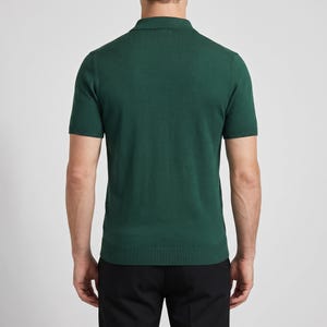 Op de afbeelding: Een donkergroen poloshirt met korte mouwen. De blouse heeft een geribbelde kraag en zoom en is gemaakt van een gebreide stof. Het model draagt een zwarte broek. De blouse is effen van kleur en heeft een klassiek ontwerp.