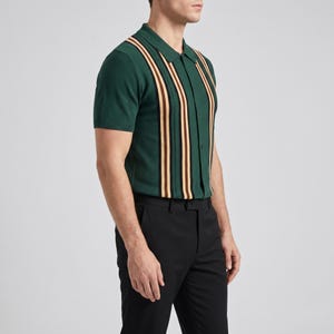 Op de afbeelding: Groen poloshirt met korte mouwen en verticale strepen in bruin, zwart en beige. Het shirt heeft een button-down kraag en wordt gecombineerd met een zwarte broek. De stijl is klassiek en preppy.