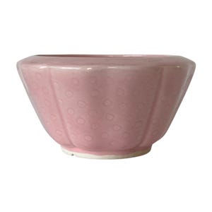 May include: A light pink ceramic bowl with a scalloped rim and a subtle embossed polka dot pattern across the exterior surface. The bowl features a wide, flared opening that tapers down to a narrow, circular base with a white unglazed foot.