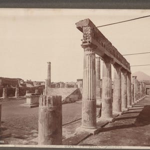 May include: A sepia-toned photograph of the ancient ruins of Pompeii, featuring a row of weathered stone columns supporting a horizontal beam. In the background, a stone staircase and additional fragmented pillars are visible under a clear sky.