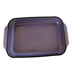 Puede incluir: Una fuente de horno rectangular de cristal morado con asas laterales integradas. El centro de la fuente presenta el nombre de la marca Pyrex en relieve. El cristal es translúcido y liso, con esquinas redondeadas y un borde ancho y plano.