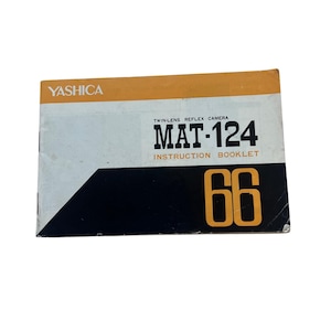 May include: A rectangular instruction booklet for a Yashica Mat-124 twin-lens reflex camera. The cover features a white background with a horizontal orange stripe at the top, a black diagonal section at the bottom, and the large orange number 66.