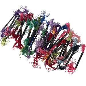 May include: A collection of embroidery floss skeins in a wide variety of colors including red, green, blue, purple, pink, yellow, and black. Each skein is secured with a black paper label featuring white text that reads Strandsheen and Boilfast.