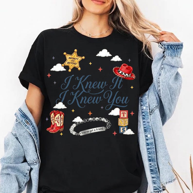 May include: A black t-shirt featuring a graphic print with the text "I Knew It I Knew You". The design includes a gold sheriff badge with "INFINITY AND BEYOND", a red cowboy hat, red boots, a silver bracelet with "You've got a friend", and blocks.