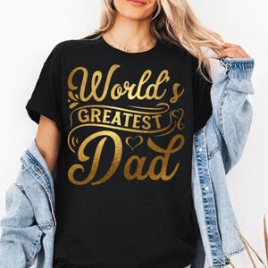 Peut inclure: Un t-shirt noir à manches courtes avec le texte doré "World's GREATEST Dad" imprimé sur le devant. Le motif comprend des fioritures décoratives et une petite icône de cœur intégrée dans le lettrage, centré sur la poitrine.