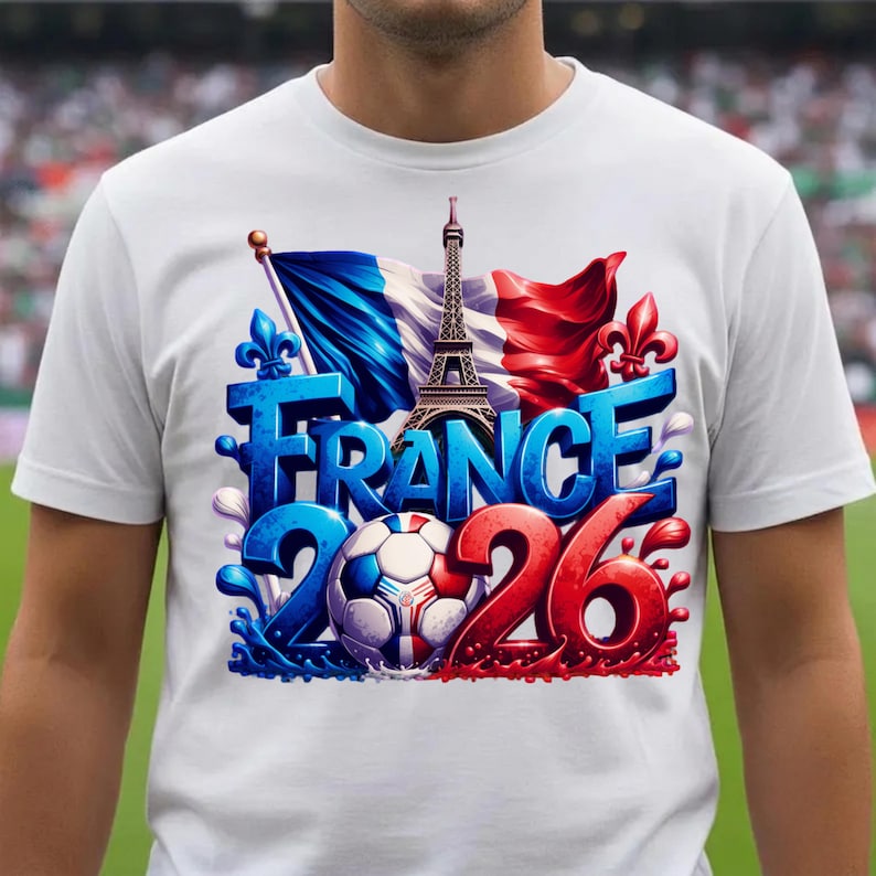 K&ouml;nnte beinhalten: Wei&szlig;es T-Shirt mit einem Grafikdesign, das Frankreich feiert. Das Design umfasst das Wort "FRANCE" in Blau, den Eiffelturm, einen Fu&szlig;ball und die Zahlen "2026" in Rot. Die franz&ouml;sische Flagge und Fleur-de-Lis sind ebenfalls abgebildet.