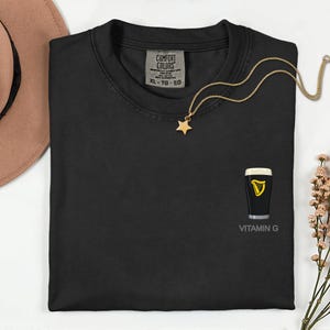a black t-shirt with a gold star pendant and a pint of Guinness beer graphic, along with a gold necklace and a brown hat.