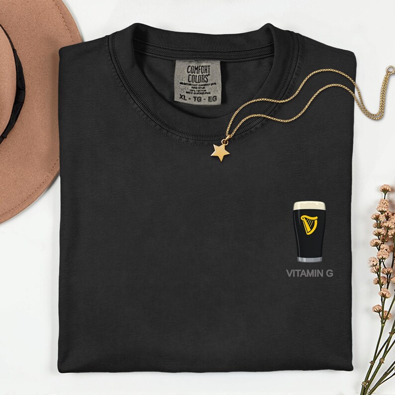 a black t-shirt with a gold star pendant and a pint of Guinness beer graphic, along with a gold necklace and a brown hat.