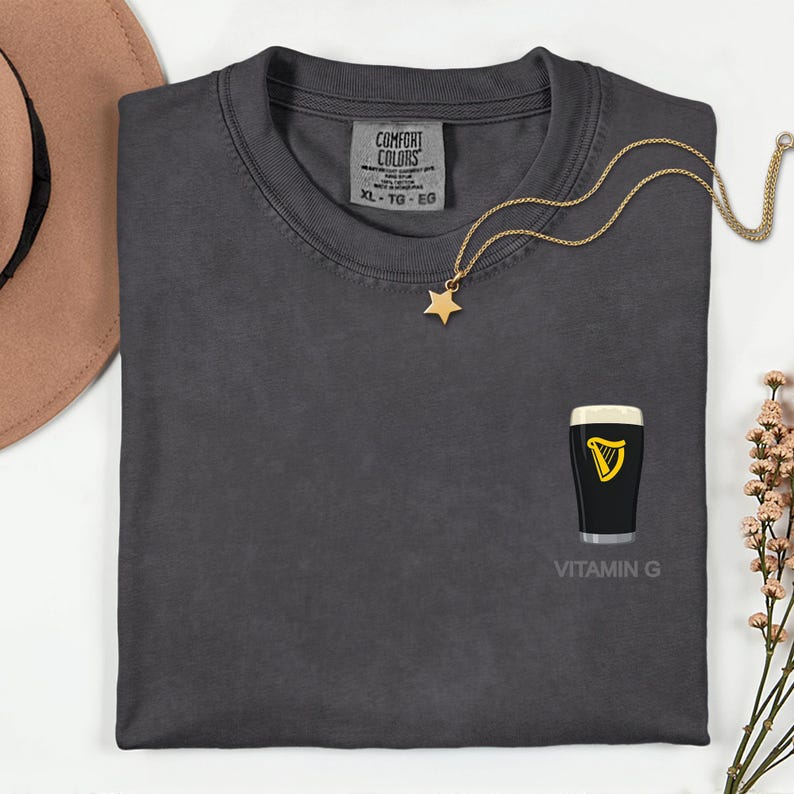 a gray t-shirt with a graphic of a pint of Guinness beer and a star-shaped charm, along with a necklace and a hat.