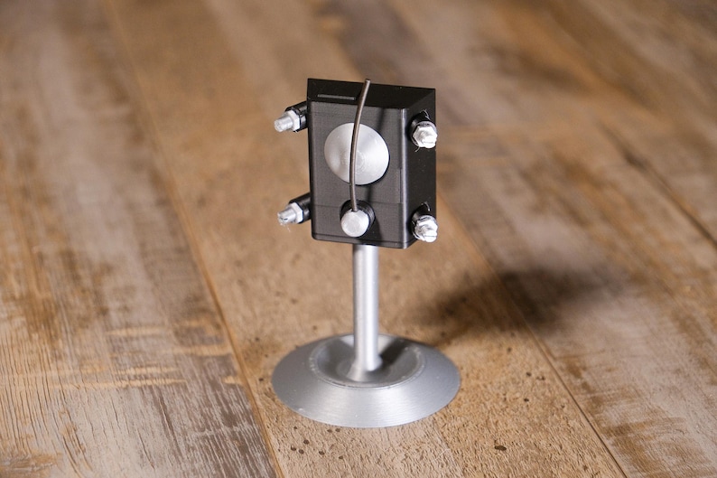 May include: A white ceramic mug with a black handle and the text "But First, Coffee" in a handwritten style. The mug is on a white surface. The mug is 10 cm tall.