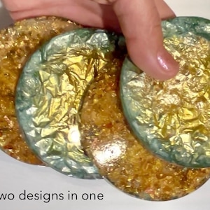 May include: Four round coasters with gold and teal accents. The coasters have a textured, metallic appearance, with gold leaf embedded in the resin. The text "Two designs in one" is visible at the bottom of the image.