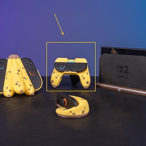 May include: A collection of yellow and black Nintendo Switch accessories, including a controller, Joy-Cons, and a dock. The controller and Joy-Cons are designed to resemble bananas, with brown spots. The dock is black with the text "SWITCH 2".
