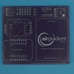 Può includere: Un circuito stampato (PCB) viola con vari componenti elettronici ed etichette di testo. La scheda presenta il logo "airgradient" e il testo "PCB v2". Include testo per sensori di CO2 e PM e microcontrollore.