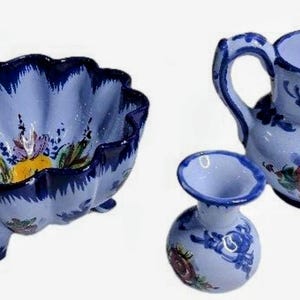 May include: A set of three ceramic pieces: a scalloped bowl with floral accents, a small pitcher, and a bud vase. The pieces are light blue with dark blue trim and hand-painted floral designs.