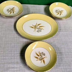 May include: A set of vintage yellow and white ceramic plates. The plates have a gold rim and a floral design in the center. The set includes a large oval platter and several smaller round plates.
