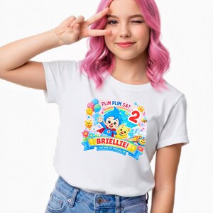 May include: A white short-sleeved t-shirt featuring a colorful graphic of the cartoon character Plim Plim, a yellow cat, a rainbow, balloons, and the text "PLIM PLIM SAY...", "BRIELLIE!", "YOU ARE SO SPECIAL!", and the number "2" in red.
