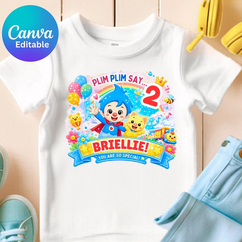 May include: A white short-sleeve t-shirt featuring a colorful graphic print of the character Plim Plim, a yellow cat, a rainbow, balloons, and a train. The text reads Plim Plim Say... 2, BRIELLIE!, and You Are So Special! in bright colors.