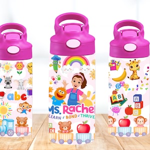 Puede incluir: Botellas de agua rosas y blancas con tapa abatible. Las botellas presentan ilustraciones coloridas de temas educativos, incluyendo el alfabeto, animales y personajes de Ms. Rachel. Las botellas están diseñadas para niños.