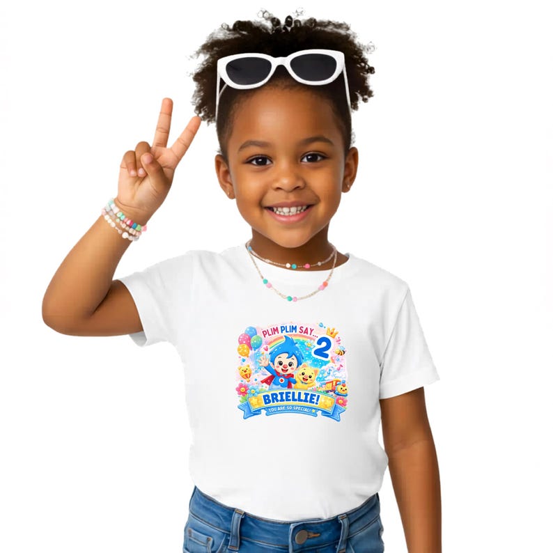 May include: A white short-sleeved t-shirt featuring a colorful graphic print of the cartoon character Plim Plim, a rainbow, balloons, and the number 2. The text reads Plim Plim Say, the name Briellie, and the phrase You Are So Special.