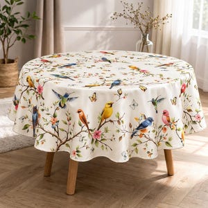 May include: A round tablecloth featuring a colorful bird and floral design. The cream-colored cloth displays various birds perched on branches with pink flowers and butterflies. The table has wooden legs.