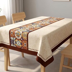 May include: A rectangular beige tablecloth with a decorative brown border and a central runner. The runner features a repeating pattern of colourful floral and geometric designs. The tablecloth is set on a wooden table.