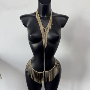 May include: Gold-toned body chain with a layered fringe design. The necklace portion cascades down the chest, and the waist chain features a similar fringe. The jewelry is displayed on a black mannequin.