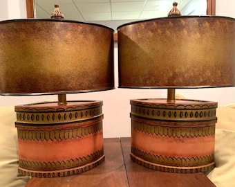 May include: Two matching table lamps with oval shades and decorative bases. The shades are a mottled gold and brown, and the bases are peach with gold and black trim. Each lamp has a gold-colored finial.