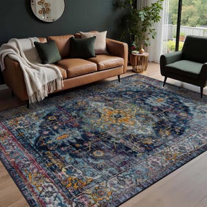 Könnte beinhalten: Ein großer, rechteckiger Teppich mit einem verzierten, verwitterten Design. Der Teppich hat ein zentrales Medaillon in Orange- und Gelbtönen, umgeben von einem marineblauen Feld mit Akzenten in Lila, Rosa und Hellblau. Der Teppich befindet sich in einem Wohnzimmer.