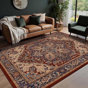 May include: A large, rectangular area rug with an intricate, traditional design. The rug features a central medallion in shades of red, beige, and blue, surrounded by a detailed border. The rug is placed in a living room setting with a brown leather sofa and green armchair.