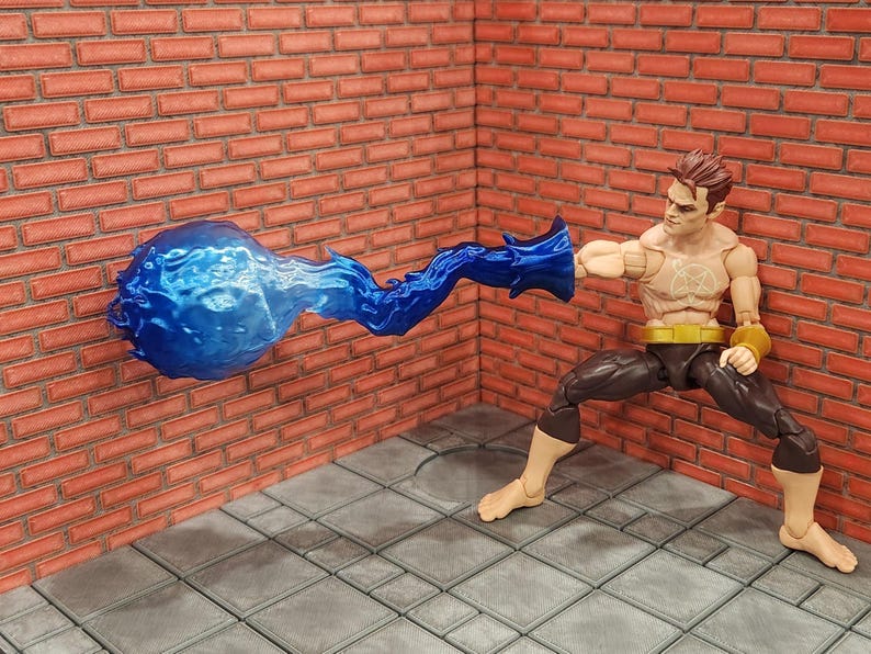 May include: A superhero action figure in a dynamic pose, with a blue energy blast emanating from his hand. The figure is wearing black pants, a yellow belt, and wristbands. The background features a brick wall and a tiled floor.