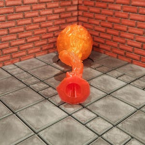 May include: An orange, abstract sculpture with a bulbous top and a flared base. The sculpture is made of a translucent material, and the background features a brick wall and a tiled floor.
