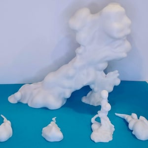 Puede incluir: Colección de esculturas abstractas blancas, que recuerdan a nubes o humo, dispuestas sobre una superficie azul. Las formas varían en tamaño y forma, con una pieza central grande y varios elementos más pequeños y separados.