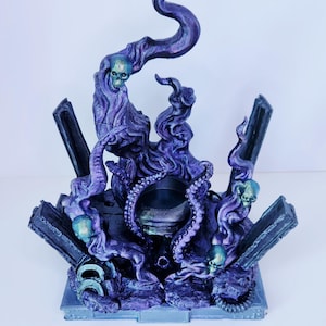 May include: A detailed, fantasy-themed sculpture in shades of purple and blue. The piece features a central, dark circular element surrounded by swirling, smoke-like forms, tentacles, and small skulls. The base includes rectangular pillars.