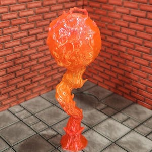 May include: A translucent orange and red decorative sculpture resembling a stylized flame. The sculpture has a bulbous top with a textured surface, supported by a swirling, flame-like stem and a flared base. The piece is set against a brick wall and a tiled floor.