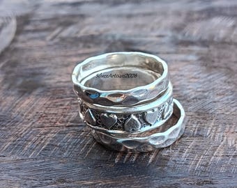 May include: A stack of three silver rings. The top and bottom rings feature a hammered, uneven texture. The middle ring displays a repeating pattern of raised hearts against a textured background. The text SilverArtisan2026 is visible inside.