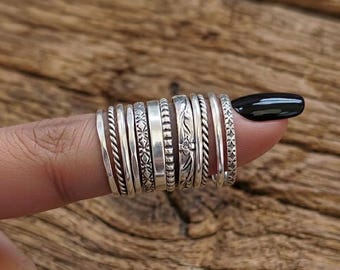Könnte beinhalten: Eine Sammlung von Silberringen mit verschiedenen Designs, darunter gedrehte Seile, Blumenmuster und geometrische Muster. Die Ringe sind auf einem Finger gestapelt und zeigen die verschiedenen Texturen und Stile. Die Ringe sind aus Silber.
