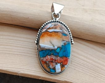 May include: An oval pendant featuring a multi-coloured stone inlay with shades of orange, turquoise, and white, set in a polished silver frame with a beaded border and a triangular bail. The text SilverArtisan2026 is visible on the stone surface.