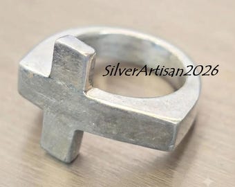 May include: A silver-toned metal ring featuring a prominent cross-shaped design integrated into the band. The surface of the ring has a matte, brushed finish. The text SilverArtisan2026 is clearly visible across the centre of the ring band.
